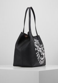 Czarna torebka typu tote z teksturowanej skóry z dwoma uchwytami, ozdobiona białym graficznym wzorem i wnętrzem w panterkę. Zaprojektowana w szerokim, luźnym kształcie.