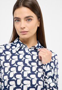 Button-up shirt featuring a geometric pattern in navy and white, crafted from smooth fabric with a structured collar and long sleeves.