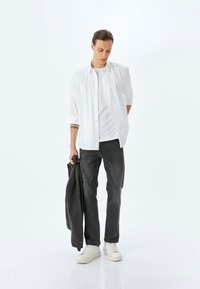 Camisa blanca de manga larga sobre una camiseta blanca, combinada con jeans grises y zapatillas blancas. Sosteniendo una chaqueta de mezclilla oscura. Diseño minimalista.