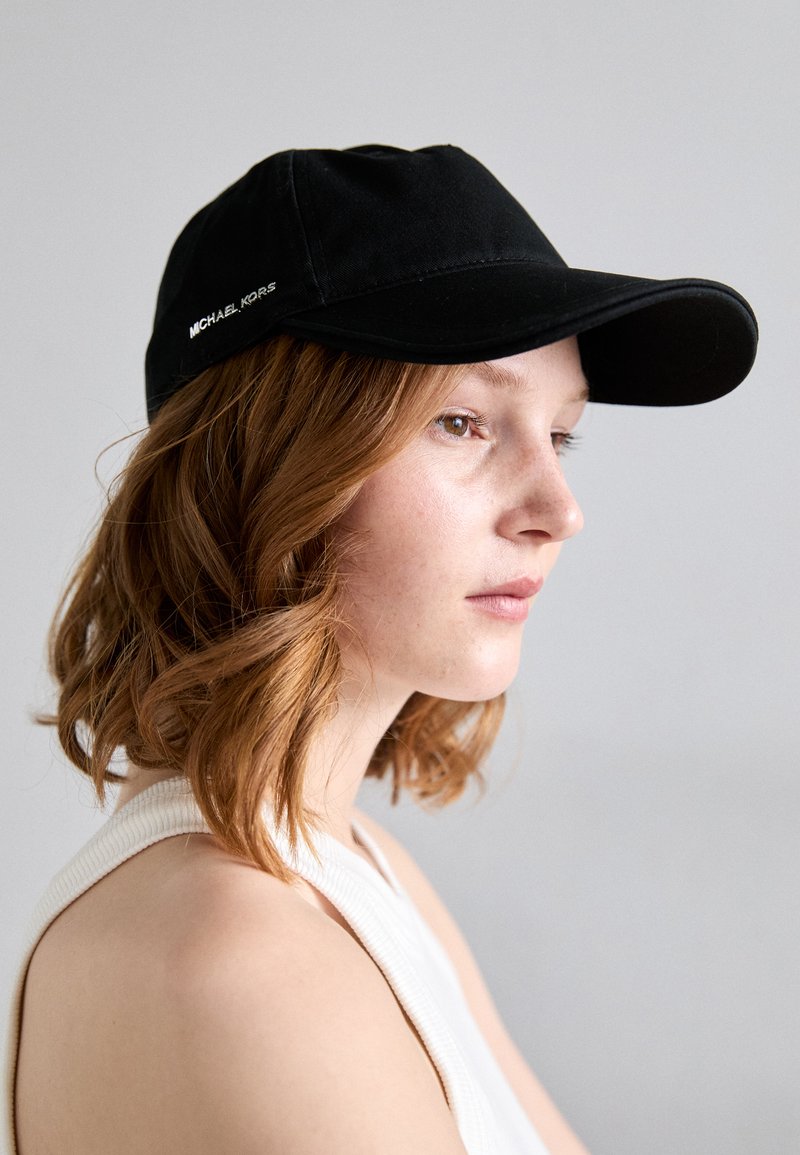 Black baseball cap featuring a curved brim and embroidered "MICHAEL KORS" logo on the side. Smooth fabric texture with a structured design.