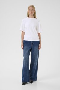 Balts kokvilnas T-krekls ar īsām piedurknēm, kopā ar brīvi pieguļošām zilām džinsa biksēm. Apģērbu papildina melni kurpes ar papēdi.