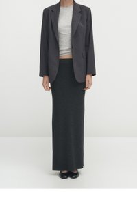 Maglietta grigia a maniche lunghe sotto un blazer grigio scuro, indossata con una gonna aderente e lunghezza caviglia. Tessuto texture e silhouette semplice.