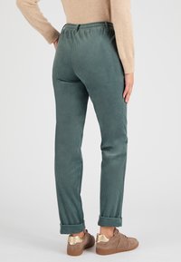Pantaloni in corduroy turchese, con un design affusolato, vita elastica e orli arrotolati. Abbinati a sneakers marroni e una maglietta beige.