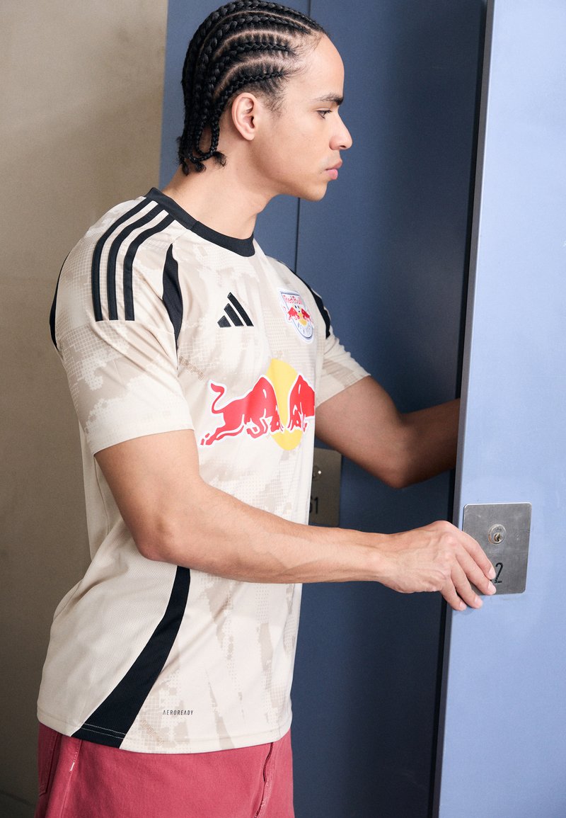 Béžový fotbalový dres s černými akcenty, s maskáčovým vzorem a logem Red Bull na přední straně. Krátké rukávy, volný střih.