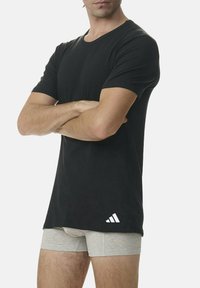Camiseta negra de manga corta en una tela suave, con un logo blanco de Adidas en el lado inferior. Combinada con bóxer de color gris claro.