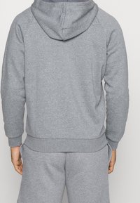 Sudadera de algodón gris con capucha, puños y dobladillo acanalados. Presenta un corte relajado y una textura suave, con costuras visibles en los hombros.
