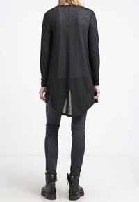 Top nero a maniche lunghe con un motivo testurizzato, orlo curvo e tessuto semi-trasparente, abbinato a jeans skinny scuri e stivaletti neri.