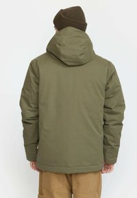 Olive green hooded jacket with a quilted texture, featuring a high collar and a straight cut. Ribbed brown beanie complements the design.
