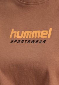 Brun bomulds T-shirt med et fremtrædende orange "hummel" logo og sort "SPORTSWEAR" tekst. Glat stoftekstur, rund halsudskæring.