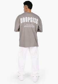 Grå oversized t-shirt med hvid, fed tekst på ryggen, parret med hvide cargo bukser og hvide sneakers. Stoffet ser blødt og afslappet ud.
