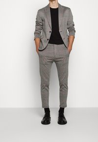 Harmaa ruudullinen puku punaisilla viivoilla, johon kuuluu muotonsa mukainen bleiseri ja slim-fit-housut, yhdistettynä mustaan T-paitaan ja mustiin juhlakengiin.