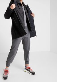 Černá zateplená bunda s předním zipem a fleecovou podšívkou, spárovaná se šedými sportovními kalhotami a barevnými sportovními botami s prodyšnými prvky.