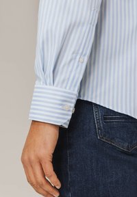 Hellblau-weiß gestreiftes Hemd mit geknöpften Manschetten, aus strukturierter Baumwolle und mit geradem Saum, kombiniert mit dunkelblauen Jeans.