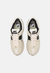 Nike Vomero 5 tenisice u bež boji s crnim naglascima, s gornjim dijelom od mrežastog materijala, vezicama i detaljima loga. Debela potplata s teksturiranim dizajnom.