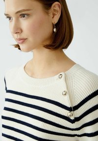 Strickpullover in Creme mit navyblauen horizontalen Streifen, verfügt über eine gerippte Textur, runden Hals und dekorative silberne Knopfakzente an der Schulter.