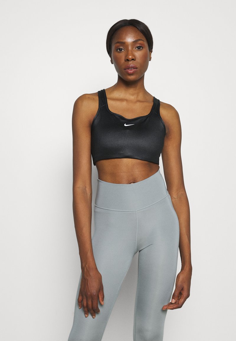 Brassière de sport noire au design élégant avec un petit logo blanc. Associée à un legging taille haute gris clair pour un contraste saisissant.