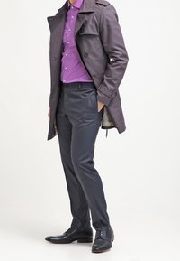 Ciemnoszary płaszcz typu trench na fioletowej koszuli na guziki, zestawiony z węglowymi spodniami i czarnymi skórzanymi butami. Gładka tkanina i dopasowany krój.