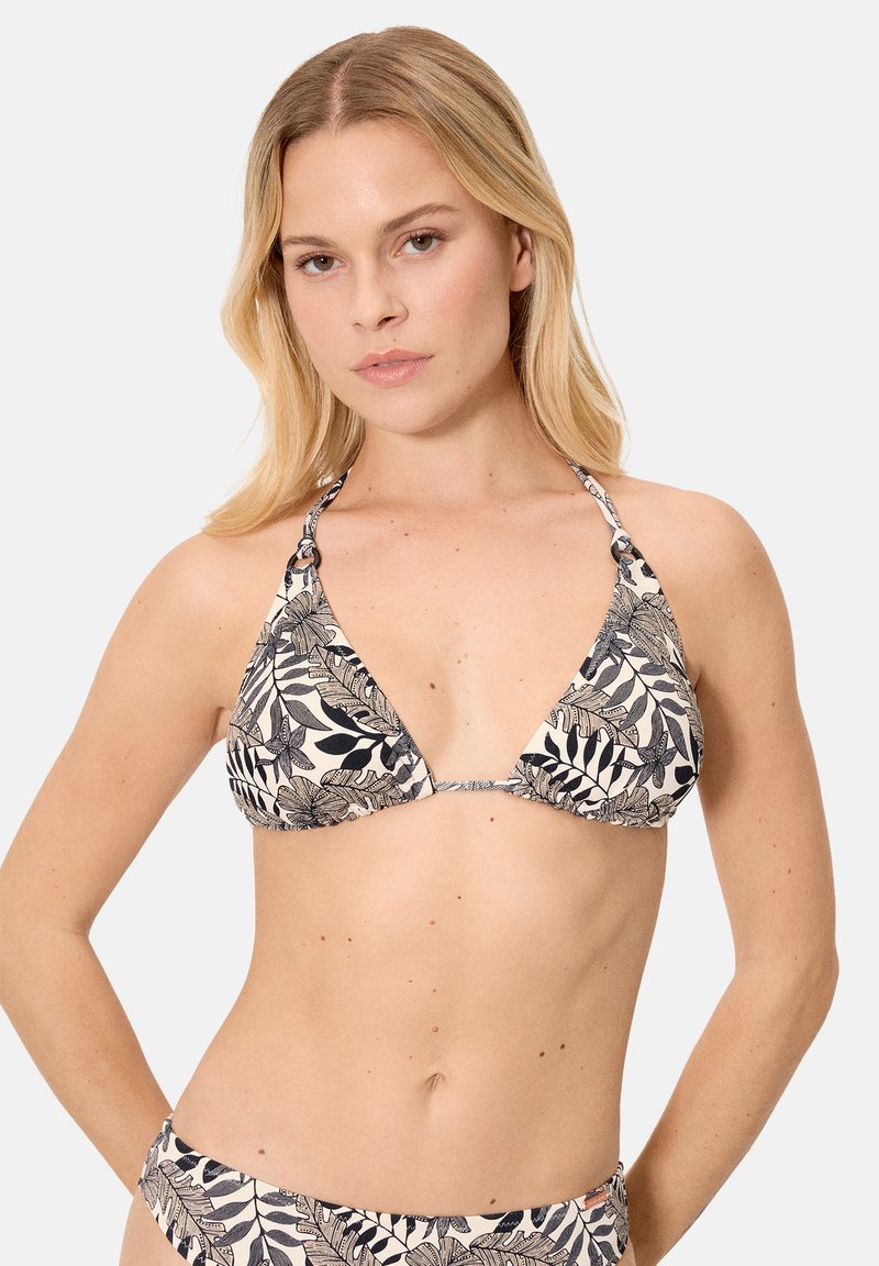 Mujer rubia con bikini de estampado tropical de hojas en blanco y negro, con top de cuello halter, sobre un fondo claro y liso.