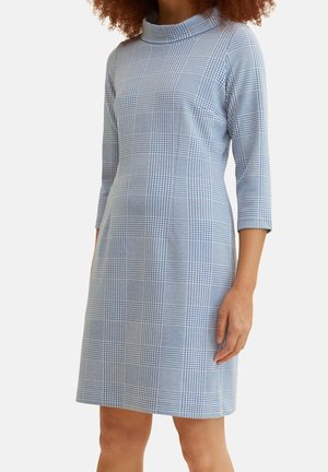 Robe à carreaux bleus avec un col haut, des manches trois-quarts et une coupe ajustée. Le tissu a une texture lisse et une silhouette structurée.