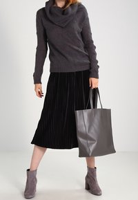 Grau cowl-neck Pullover, schwarzer plissierter Midirock, graue Leder-Tote und graue Ankle Boots mit Blockabsätzen. Schlichte, elegante Silhouette.