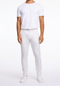 Bílé tričko kombinované s světle barevnými, úzkými kalhotami. Látka působí hladce s jemnou texturou. Obuv tvoří bílé tenisky.