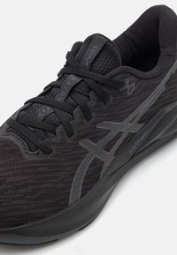Chaussure de sport noire avec une tige en maille, surface texturée et accents de marque discrets. La semelle est rembourrée pour un confort optimal.