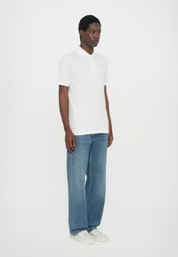 Hvit polo-skjorte med krage, kombinert med lyseblå vide jeans og hvite sneakers. Enkelt design med minimale detaljer.
