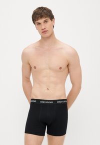 Musta puuvillainen bokserialushousut leveällä elastisella vyötärönauhalla, jossa on valkoisin kirjaimin brändinimi "ONLY & SONS". Yksinkertainen muotoilu, tiukka istuvuus.