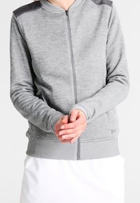 Felpa grigia chiara con zip, dettagli neri sulle spalle, polsini e orlo a coste, caratterizzata da una texture morbida e una vestibilità ergonomica.