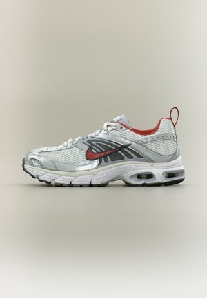 Chaussure de running Nike blanche et argentée avec des accents rouges, logo noir, tige en mesh respirant et semelle rembourrée sur fond neutre.
