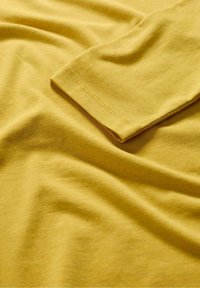 Kollane puuvillakangas, millel on sile tekstuur ja kerge venivus. Varruka äär on puhta viimistlusega ning selles on peened õmblusdetailid.