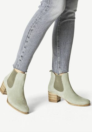 Gröna mockasnörstövlar med strukturerade nätpaneler på sidorna, spetsig tå och en staplad träklack, kombinerat med grå figurnära jeans.