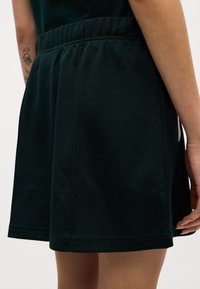 Los pantalones cortos de algodón negros cuentan con una cinturilla elástica, bolsillos en las costuras laterales y una textura suave. El diseño tiene un corte relajado y bordes dobladillados.