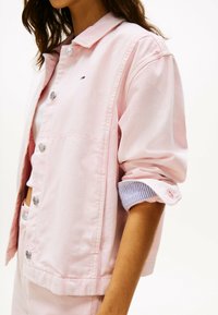 Giacca in denim rosa chiaro con bottoni argentati, dettaglio a maniche a righe e vestibilità rilassata. Presenta un emblema sul petto.