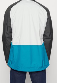 Lightweight jacket with a color-block design featuring a white upper, black sleeves, and a turquoise lower section. Smooth texture, casual fit.