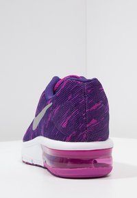 Fialová atletická bota s texturovaným síťovaným svrškem, který má růžové akcenty, šedé logo Nike a průhlednou vzduchovou tlumicí podrážku.