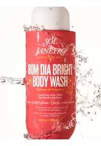 Botella de Red Sol de Janeiro Bom Dia Bright Body Wash salpicada con agua sobre un fondo blanco.