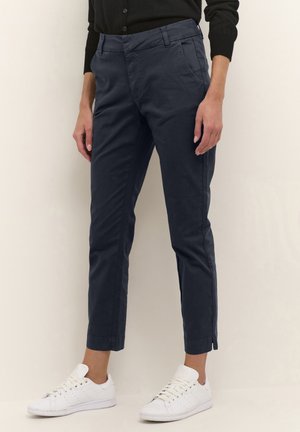 Chinos bleu marine à coupe slim, avec poches avant, devant plat et détails zippés aux poignets, associés à des baskets blanches.