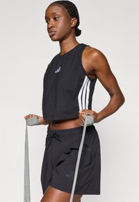 Čierny skrátený top s tromi bielymi pruhmi na stranách, kombinovaný s čiernymi šortkami s elastickým pásom a jemným brandingom.