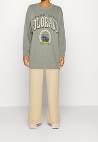 Felpa grigia chiara con grafica "Grand Lake Colorado", abbinata a pantaloni beige a gamba larga. Vestibilità rilassata, polsini a coste, tessuto morbido.