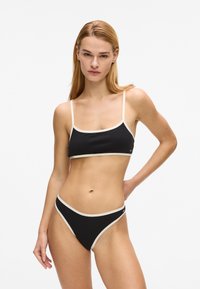 Ensemble bikini noir composé d'un haut court à fines bretelles avec des bords clairs contrastants, associé à un bas de bikini taille haute aux découpes prononcées. Texture lisse.
