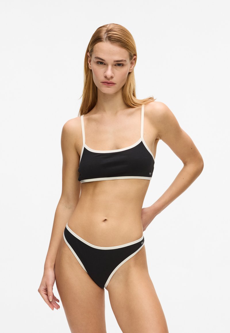 Ensemble bikini noir composé d'un haut court à fines bretelles avec des bords clairs contrastants, associé à un bas de bikini taille haute aux découpes prononcées. Texture lisse.
