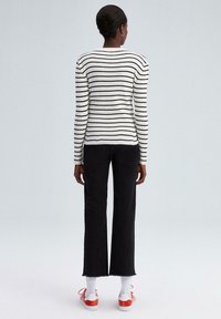 Zwart-wit gestreepte ribgebreide trui, slim fit, lange mouwen, gecombineerd met zwarte wijde broek en rode sneakers met witte sokken.