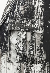 Črno-bela vzorčasta tkanina z abstraktnimi teksturami, z črno etiketo s napisom "Carlo Colucci", prišito na žep.