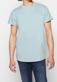 Ljusblå t-shirt med rund hals, tillverkad av mjukt bomullstyg, med korta ärmar och en liten logga på bröstet. Avslappnad passform.