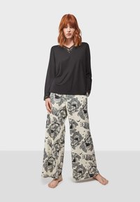 Haut noir à manches longues avec des détails en dentelle au niveau du col, associé à un pantalon large présentant un motif floral et de hiboux sur un fond crème.