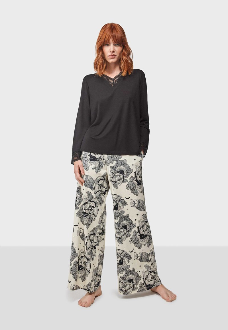 Haut noir à manches longues avec des détails en dentelle au niveau du col, associé à un pantalon large présentant un motif floral et de hiboux sur un fond crème.