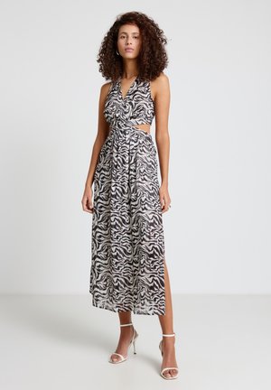 Donna in piedi in un vestito midi senza maniche con stampa zebra bianca e nera, con taglio laterale e spacco, che indossa sandali bianchi con tacco alto.