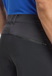 Pantaloni sportivi neri con una texture liscia, dotati di una tasca con zip sul retro e cordini regolabili in vita.