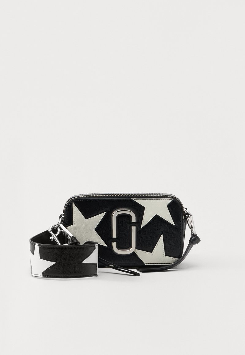 Geantă cu fermoar alb-negru, având modele mari de stele, un logo argintiu proeminent și o curea detașabilă decorată cu stele asortate.